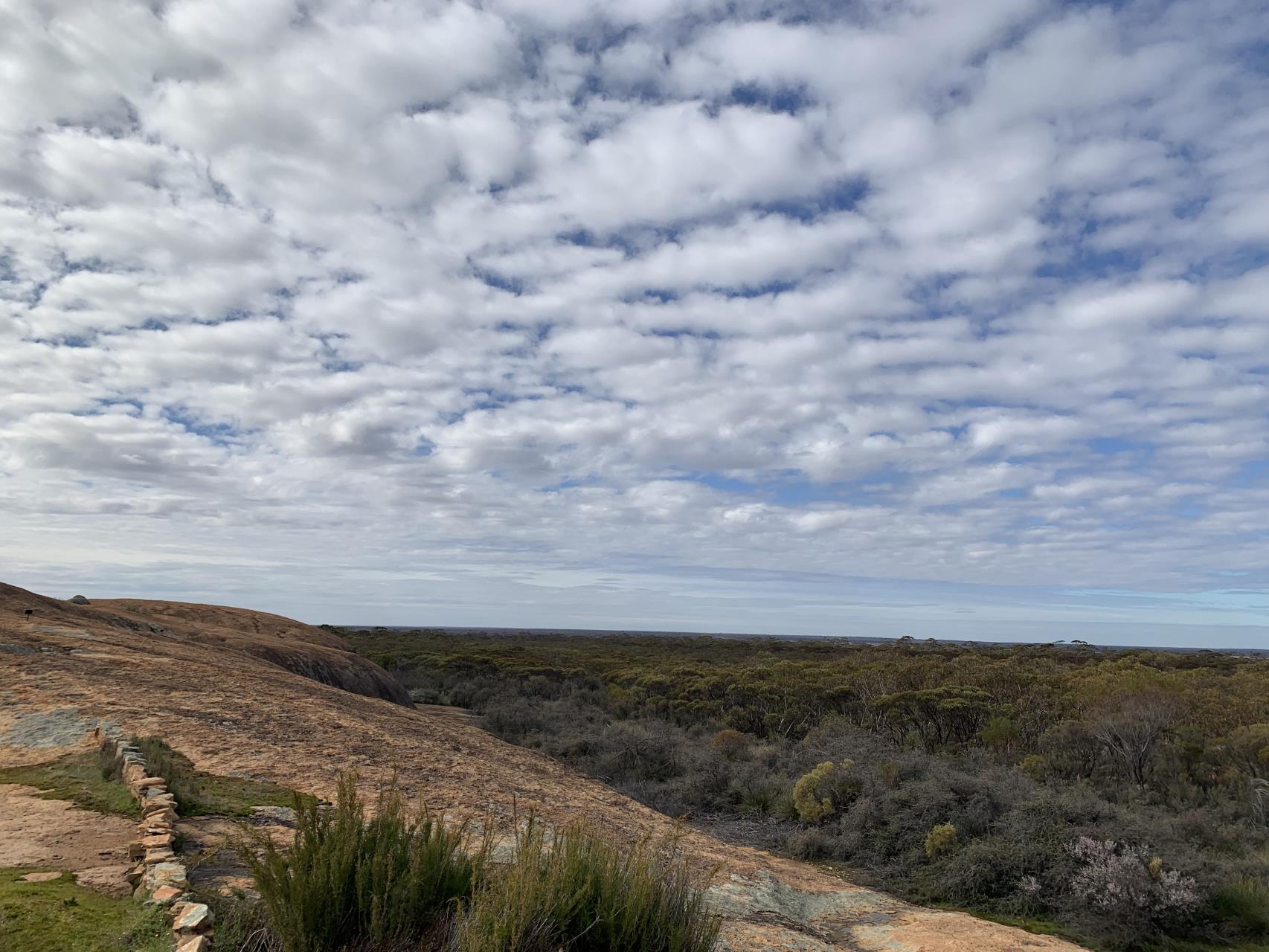 A scenic photo taken along the trail and showing clouds, a bluie sky and a large rock