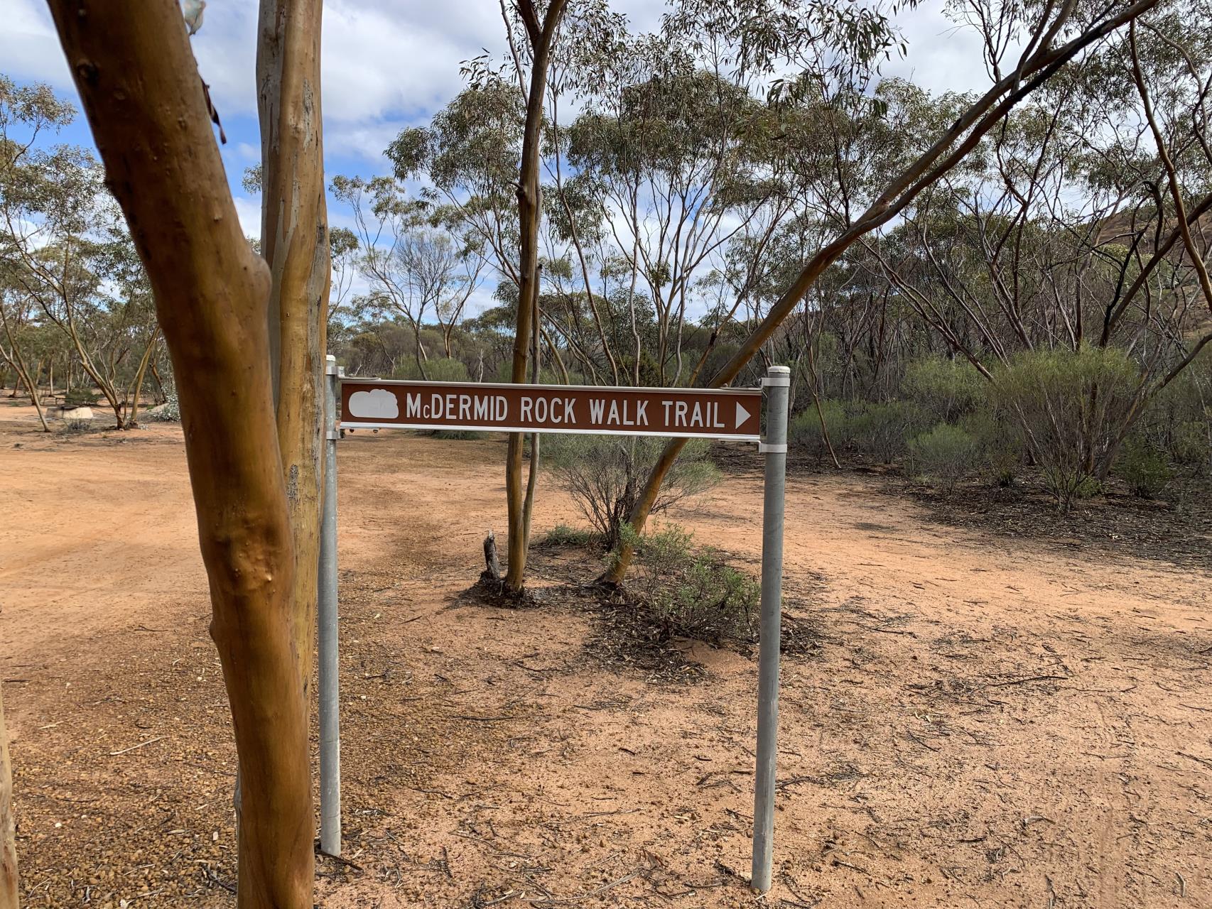 A sign along a dirt track amongst some trees directs visitors towards the McDermid Rock Walk Trail.